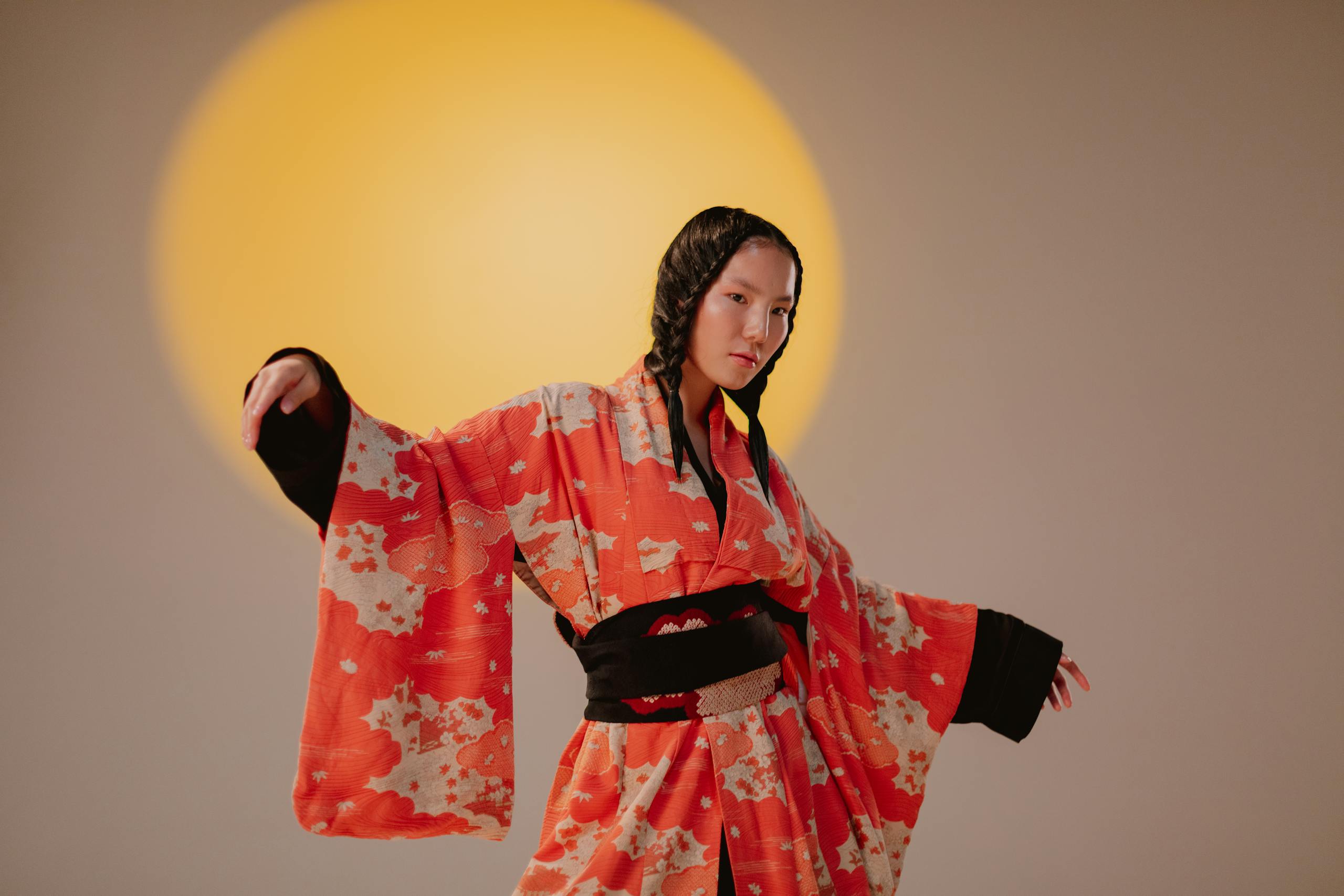A young woman gracefully poses in a vibrant Japanese kimono under a studio spotlight.